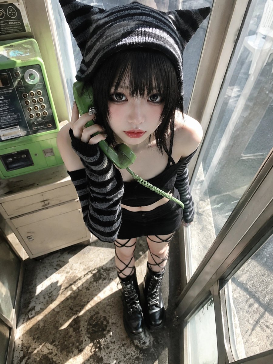 A young adult woman crouching inside a retro public phone bo